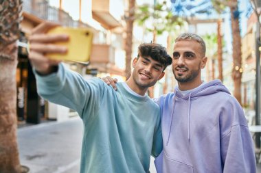 Genç eşcinsel çift mutlu bir şekilde gülümsüyor. Şehirdeki akıllı telefonun yanında selfie çekiyorlar..
