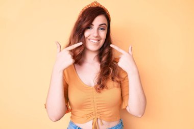 Genç ve güzel bir kadın günlük kıyafetler giyip neşeli bir şekilde gülümsüyor ve parmaklarıyla ve ağzıyla işaret ediyor. diş sağlığı kavramı. 