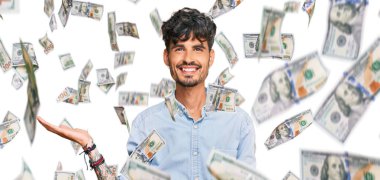 Gündelik kıyafetler giyen genç İspanyol adam neşeli bir şekilde gülümsüyor ve avuç içi kameraya bakıyor..