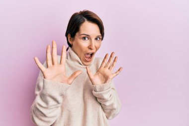 Kısa saçlı, kısa saçlı, kışlık süveter giyen, korku ifadesinden korkan genç esmer kadın. El hareketini durdur, şok içinde bağır. panik konsepti. 