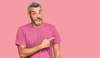 Orta yaşlı, gri saçlı, günlük kıyafetler giyen bir kenara endişeli ve gergin bir adam işaret parmağıyla endişeli ve şaşırmış bir ifade takınıyor. 