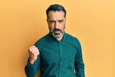 Orta yaşlı, sakallı, gri saçlı, iş kıyafetleri giyen öfkeli ve kızgın bir şekilde yumruğunu kaldıran öfkeli bir adam. öfke ve agresif konsept. 