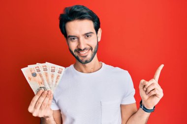 İspanyol asıllı genç adam, elinde 10 pound tutuyor. Banknotlar, gülümsüyor, mutlu bir şekilde işaret ediyor. 