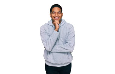 Sıradan bir tişört giyen genç, yakışıklı İspanyol adam kameraya kendinden emin bakıyor kollarını kavuşturmuş ve çenesini kaldırmış şekilde gülümsüyor. Olumlu düşünmek. 