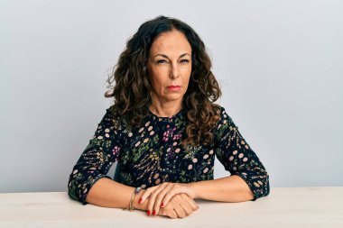 Gündelik kıyafetler giyen orta yaşlı güzel bir kadın şüpheci ve gergin bir şekilde masada oturuyor, sorun yüzünden suratını asıyor. negatif kişi. 