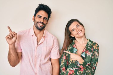 Güzel bir çift genç sevgili birlikte gülümsüyor ve kameraya bakıyor iki eliyle ve parmaklarıyla kenarı işaret ediyor.. 