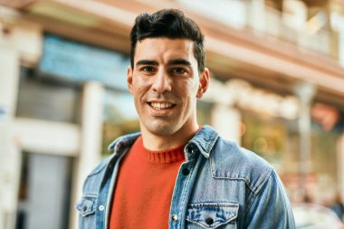 Genç İspanyol adam gülümseyerek şehirde mutlu mesut dikiliyor..