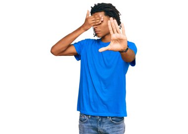 Genç, Afro-Amerikan bir adam, günlük kıyafetler giyiyor, elleriyle gözleri örtüyor ve üzgün ve korku ifadeleriyle jestleri durduruyor. utangaç ve olumsuz kavram. 
