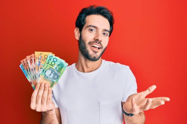 Avustralya doları tutan genç İspanyol adam başarıyı mutlu bir gülümsemeyle kutluyor ve kazanan el kaldırarak ifade ediyor. 