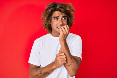 Gündelik beyaz tişört giyen genç İspanyol adam gergin ve gergin görünüyor. Ağzı tırnak yiyen eller. anksiyete. 