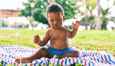 Sevimli Afro-Amerikan çocuk parkta çimlerin üzerinde oturuyor..