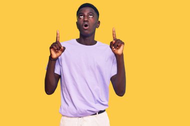 Gündelik giysiler giyen genç Afro-Amerikan adam şaşkın ve şaşırmış bir şekilde yukarı baktı ve parmaklarıyla işaret etti ve kollarını kaldırdı.. 
