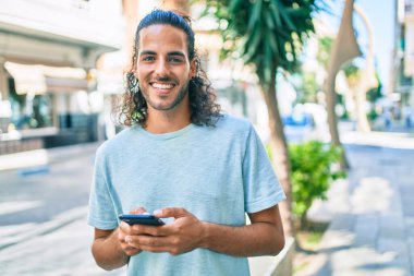 Genç İspanyol adam şehirde akıllı telefon kullanarak mutlu gülümsüyor..