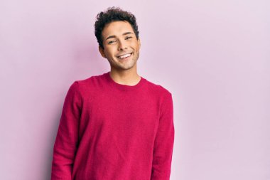Yakışıklı, İspanyol bir adam pembe arka planda günlük kıyafetler giyiyor ve yüzünde güzel bir gülümseme var. şanslı kişi. 