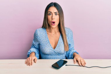 Gündelik kıyafetler giyen genç İspanyol kadın akıllı telefonun şarjını dolduruyor. Şaşırmak için ağzı açık kalmış, korkmuş ve şaşırmış. 