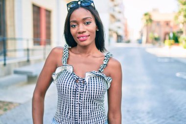 Genç Afrikalı Amerikalı kadın gülümsüyor. Şehrin caddesinde mutlu bir şekilde yürüyor.