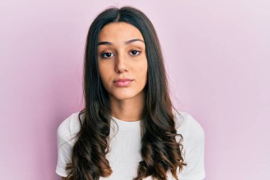 Yüzünde ciddi bir ifade olan günlük beyaz tişört giyen genç İspanyol kadın. Basit ve doğal bir şekilde kameraya bakıyorsun.. 