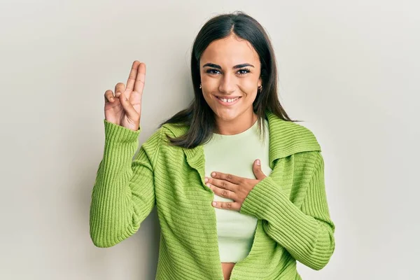 Young brunette woman wearing casual clothes smiling swearing with hand on chest and fingers up, making a loyalty promise oath
