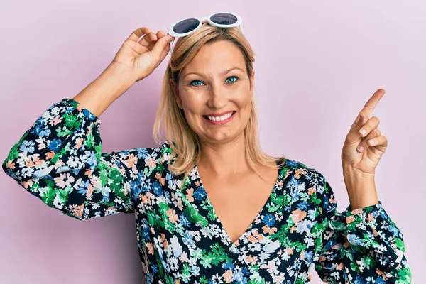 Orta yaşlı, beyaz, çiçekli gömlek ve güneş gözlüğü takan bir kadın gülümsüyor. 