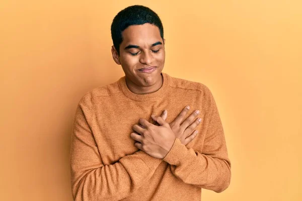 目を閉じて胸の上で手で笑みを浮かべてカジュアルな冬のセーターを着て若いハンサムなヒスパニック系の男と顔に感謝のジェスチャー 健康の概念 — ストック写真