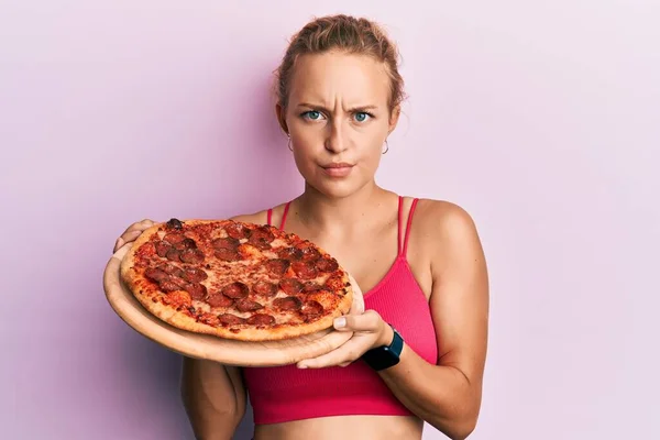 漂亮的高加索女人带着意大利披萨的怀疑和紧张 皱着眉头因问题而烦恼 消极的人 — 图库照片