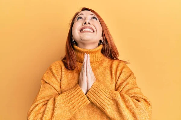 Beautiful redhead woman wearing casual winter sweater over yellow background begging and praying with hands together with hope expression on face very emotional and worried. begging.