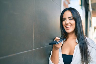 Genç İspanyol kız gülümseyerek şehirde akıllı telefon kullanarak sesli mesaj gönderiyor..
