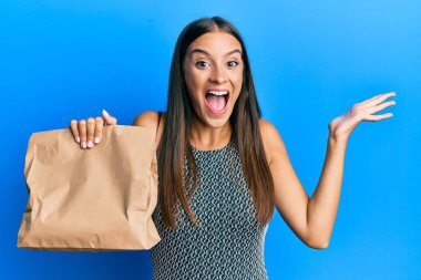 Elinde kağıt torba tutan genç İspanyol kadın zaferi mutlu bir gülümsemeyle ve ellerini kaldırarak kutluyor. 