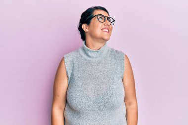 Artı, sıradan kıyafetler giyen ve gözlüklü esmer kadın yüzünde gülümsemeyle yan yana bakıyor, doğal bir ifade. Kendinden emin gülen. 