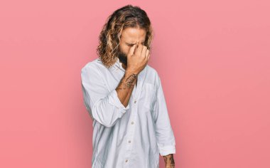 Sakallı, uzun saçlı, günlük kıyafetler giyen, burnu ve gözleri ovuşturan, yorgunluk ve baş ağrısı çeken yakışıklı bir adam. Stres ve hüsran kavramı. 