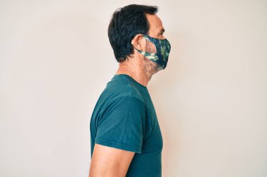 Orta yaşlı İspanyol adam, koruma maskesi takıyor. Yan tarafa bakıyor, rahat poz veriyor, kendine güveni tam bir gülümseme takınıyor.. 