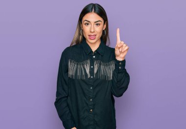 Genç İspanyol kadın gündelik kıyafetler giyip bir numarayı gösterip işaret ederken kendinden emin ve mutlu bir şekilde gülümsüyor.. 