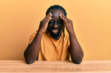 Yakışıklı, gündelik giysiler giyen genç bir adam. Kafası ağrıdığı için eli başının üstünde masada oturuyor. migren ağrısı. 