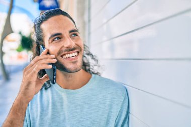 Genç İspanyol adam gülümsüyor. Akıllı telefonda konuşuyor. Duvara yaslanıyor.