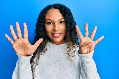 Gündelik kıyafetler giyen genç Latin kadın dokuz numaralı parmaklarını gösterip işaret ederken kendine güvenen ve mutlu gülümseyen.. 