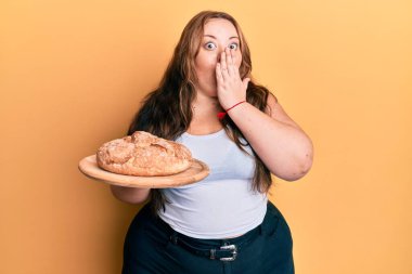 Ayrıca eli ekmeği tutan beyaz bir kadın. Ağzını kapatmış. Şok olmuş ve hata yapmaktan korkuyor. şaşırmış ifade 