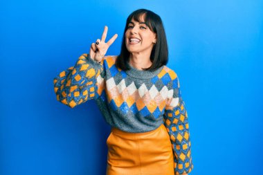 Gündelik kazak giyen genç İspanyol kadın iki numarayı gösterip işaret ederken kendine güvenen ve mutlu bir şekilde gülümsüyor.. 