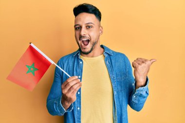 Genç Arap adam elinde Fas bayrağı, baş parmağını yana kaldırmış, ağzı açık gülümsüyor. 