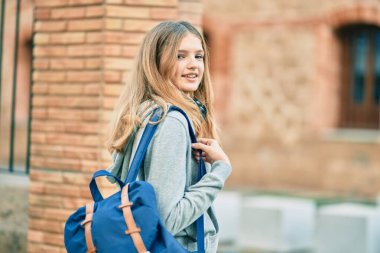 Güzel beyaz öğrenci üniversitede kulaklık takarak mutlu gülümsüyor..