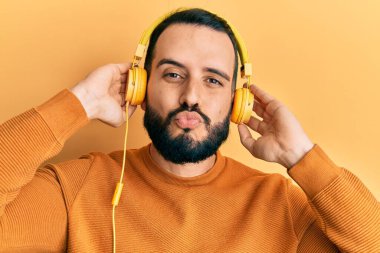 Sakallı, müzik dinleyen, kulaklık takan, kameraya bakıp öpüşen, güzel ve seksi bir genç. aşk ifadesi. 