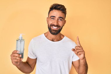 Genç İspanyol bir adam el dezenfektanı jeli kullanıyor. Bir fikir ya da soruyla gülümsüyor. Mutlu bir yüzle işaret ediyor. 