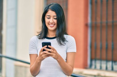 Genç İspanyol kadın şehirde akıllı telefon kullanarak mutlu bir şekilde gülümsüyor..