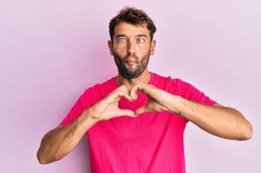 Sakallı yakışıklı adam, elleri şekilli kalp sembolü yapıyor. Ağızlı balık suratı, şaşı gözler, çılgın ve komik.. 