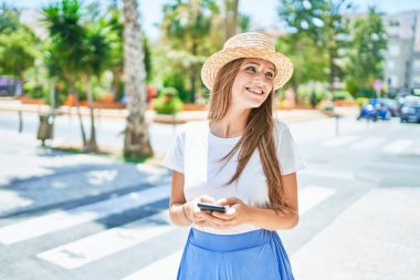 Genç sarışın kadın tatilde gülümsüyor. Şehrin caddesinde akıllı telefon kullanıyor.