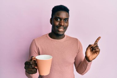 Yakışıklı siyah adam bir fincan kahve içiyor gülümsüyor mutlu bir şekilde el ve parmak kenarı gösteriyor. 