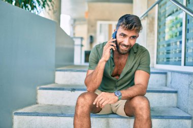 Genç İspanyol adam merdivenlerde otururken mutlu bir şekilde gülümsüyor.