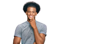 Afro saçlı, sıradan kıyafetler giyen, kameraya kendinden emin, kollarını kavuşturup gülümseyen ve çenesini kaldıran Afro-Amerikan bir adam. Olumlu düşünmek. 