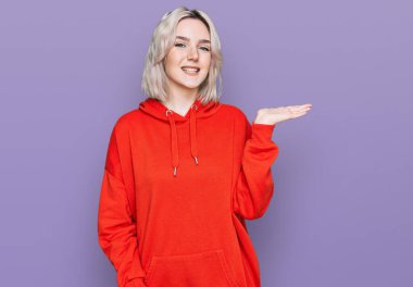 Gündelik kıyafetler giyen neşeli bir şekilde gülümseyen ve avuç içi kameraya bakan genç sarışın kız.. 