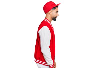 Sakallı genç adam beyzbol üniforması giyiyor. Tarafını arıyor. Profil pozu veriyor.. 