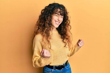 Gündelik kıyafetler giyen genç İspanyol kız başarı için heyecanlı kolları havada ve gözleri kapalı zaferi kutlarken gülümsüyor. Kazanan konsept. 